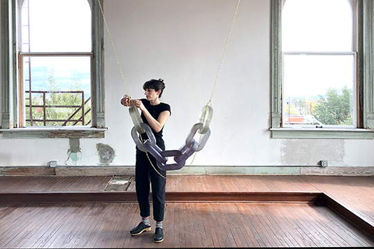 woman in black outfit adjusting hanging sculpture in an artist studio