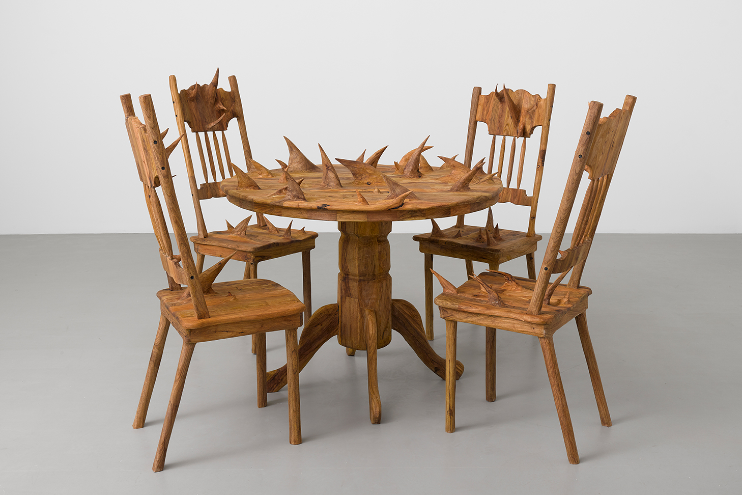 installation image of wood sculpture of four chairs and a circle dining table