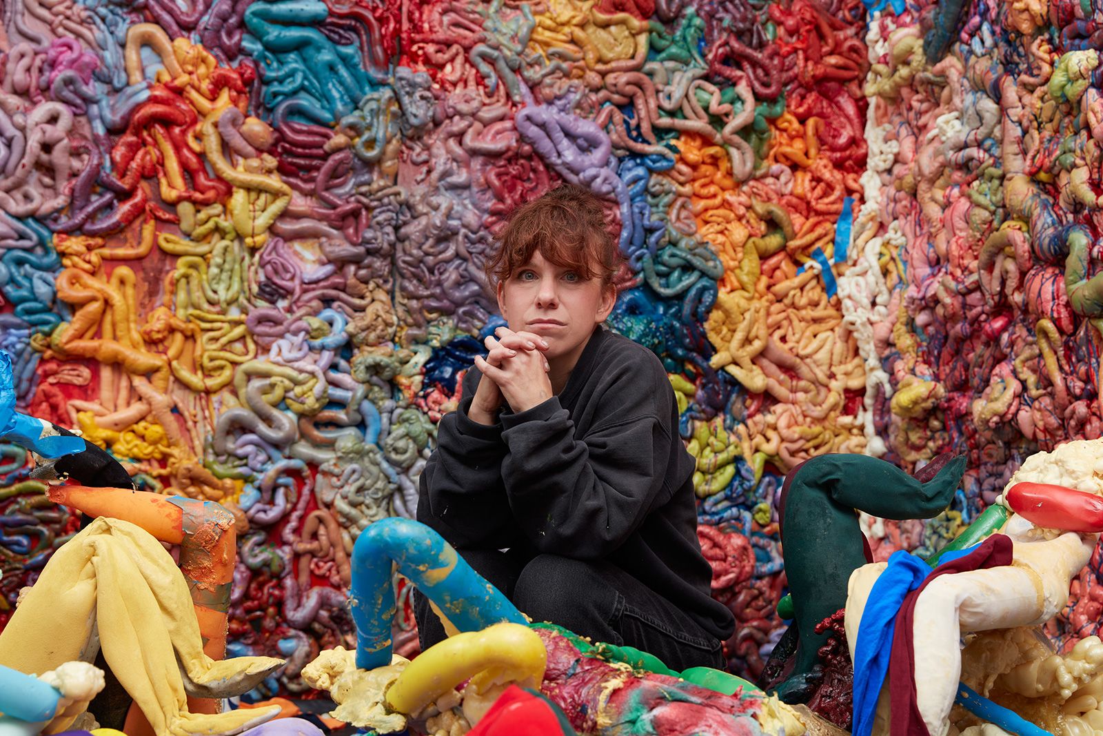 A woman sits in front of sculptures that look like colorful intestines