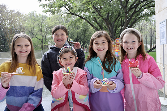 A group of girls hold up art projects in the Nasher garden